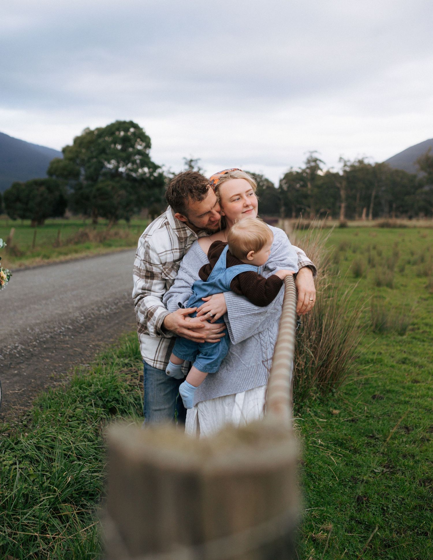 Loving family embracing by a fence on a scenic country road with mountains in the background.