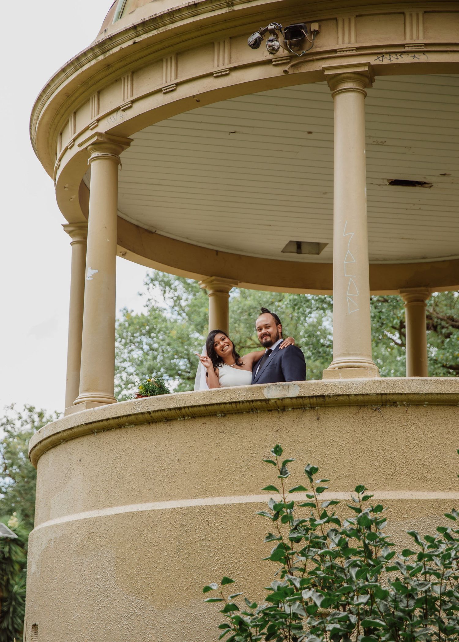 Bride and groom smiling from inside a classic rotunda gazebo structure.