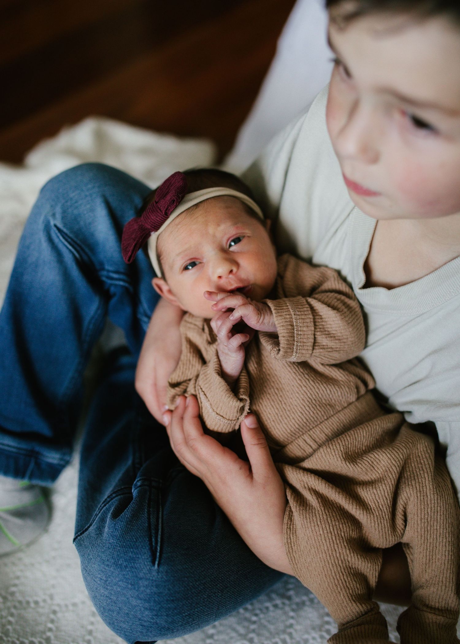 Older sibling gently holding a newborn baby girl wearing a burgundy bow headband.