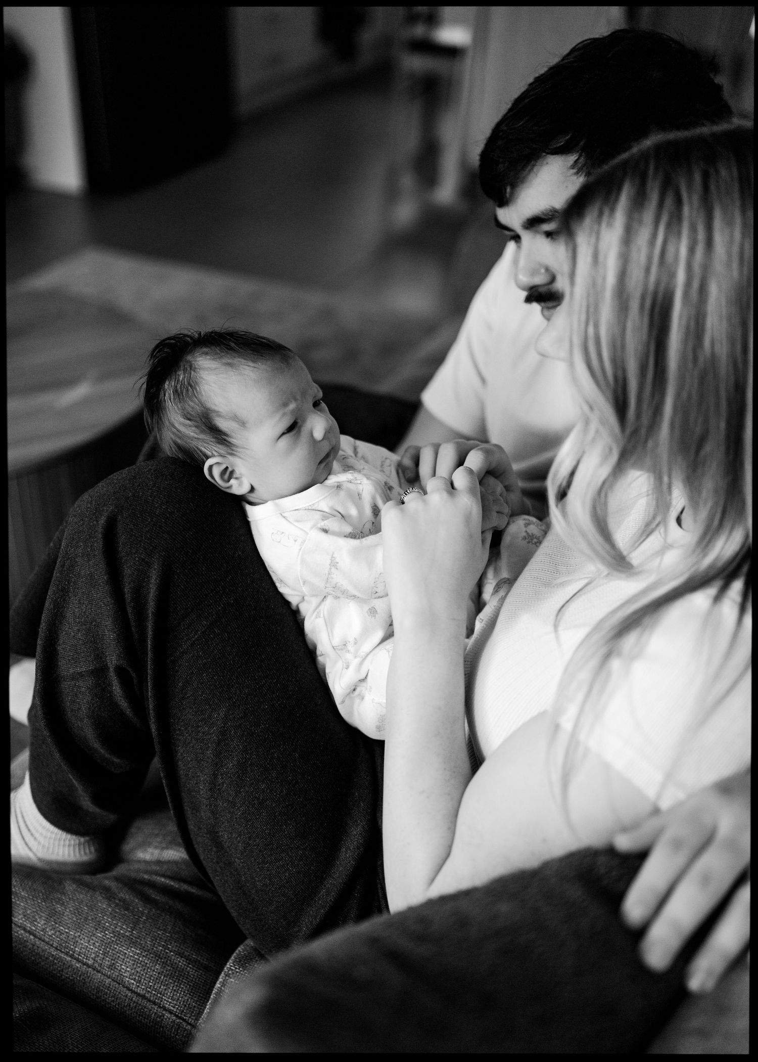 Black and white portrait of a mother and father softly holding their sleepy newborn baby during an intimate home lifestyle session.