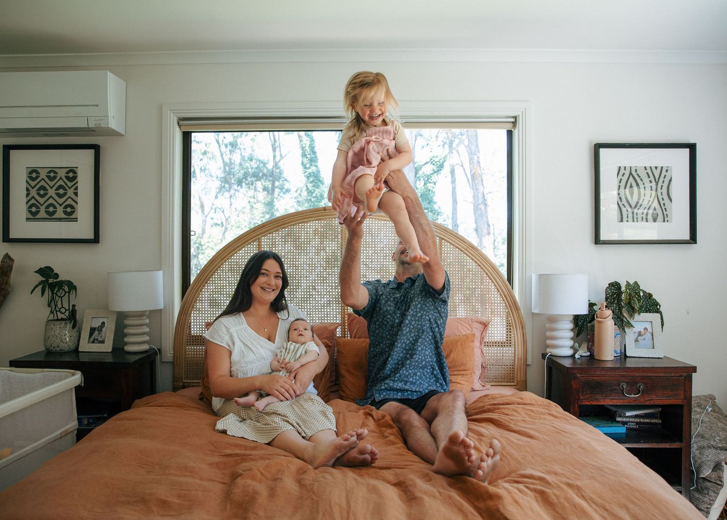 Family with newborn baby and toddler girl playing on an orange bed at home.
