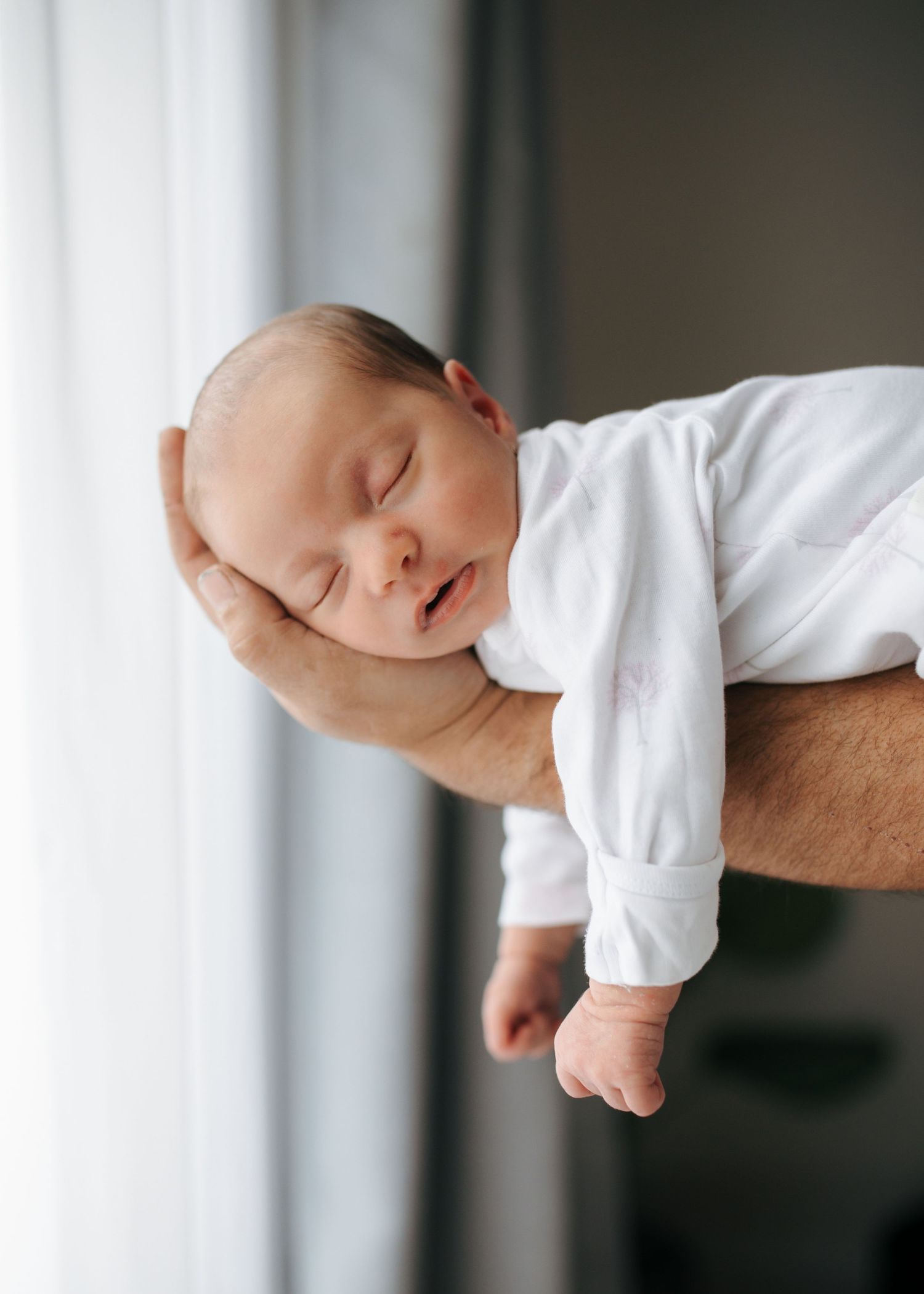Sleeping newborn baby cradled gently in father's hand wearing white onesie.