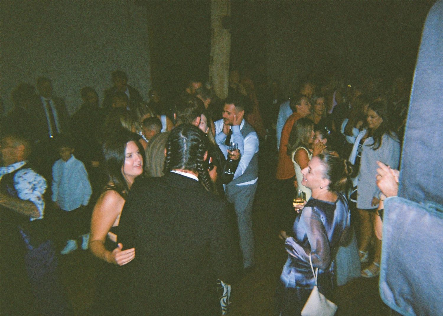Guests dancing and socializing in a dimly lit indoor wedding reception venue.