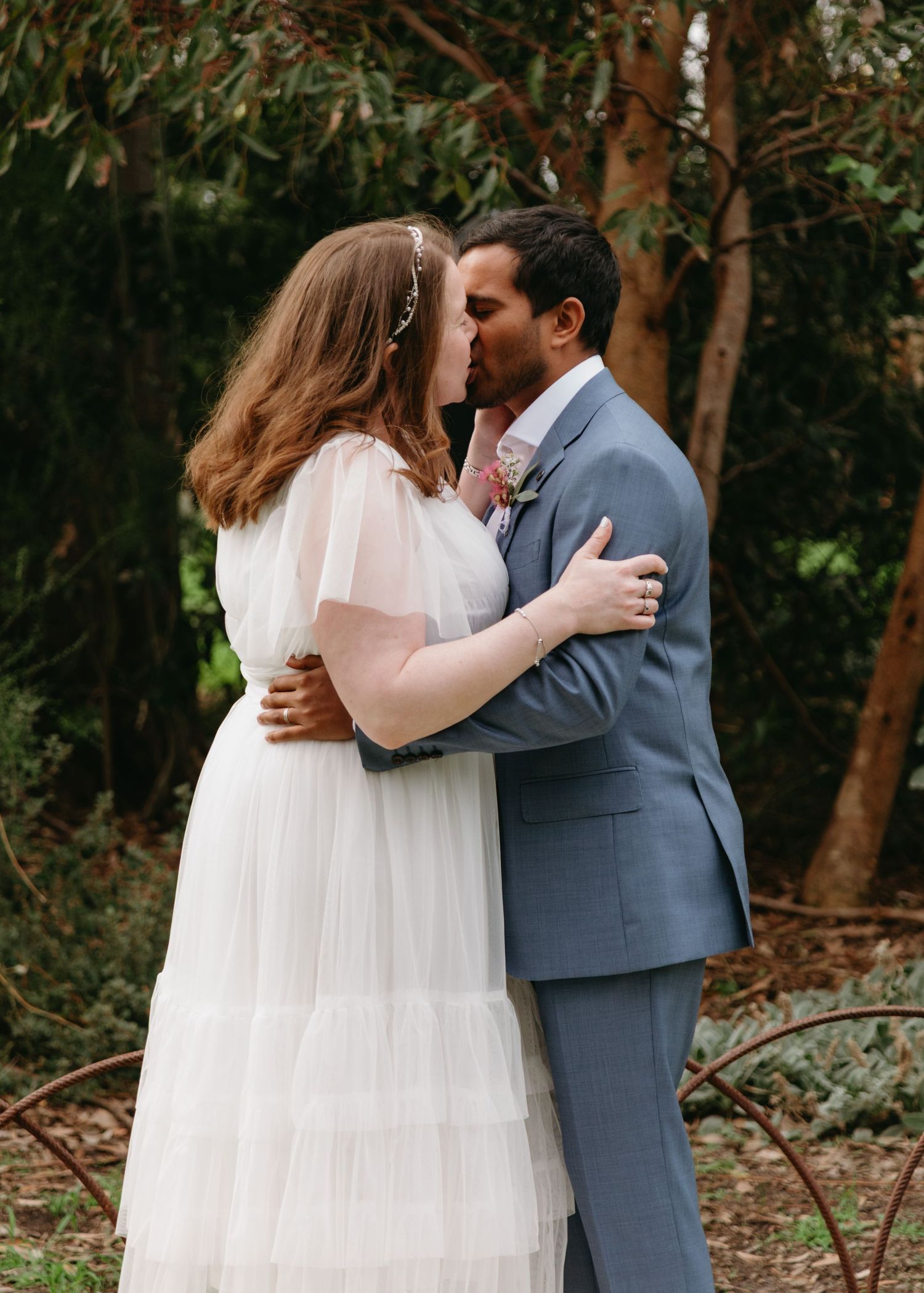 Bride and groom share first kiss surrounded by lush greenery at outdoor wedding.
