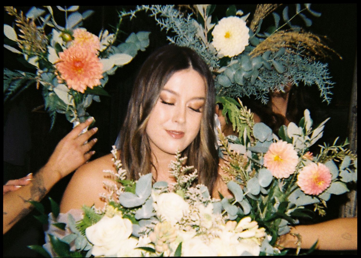 Close-up of bride wearing floral crown holding a bouquet of peach and white wedding flowers.