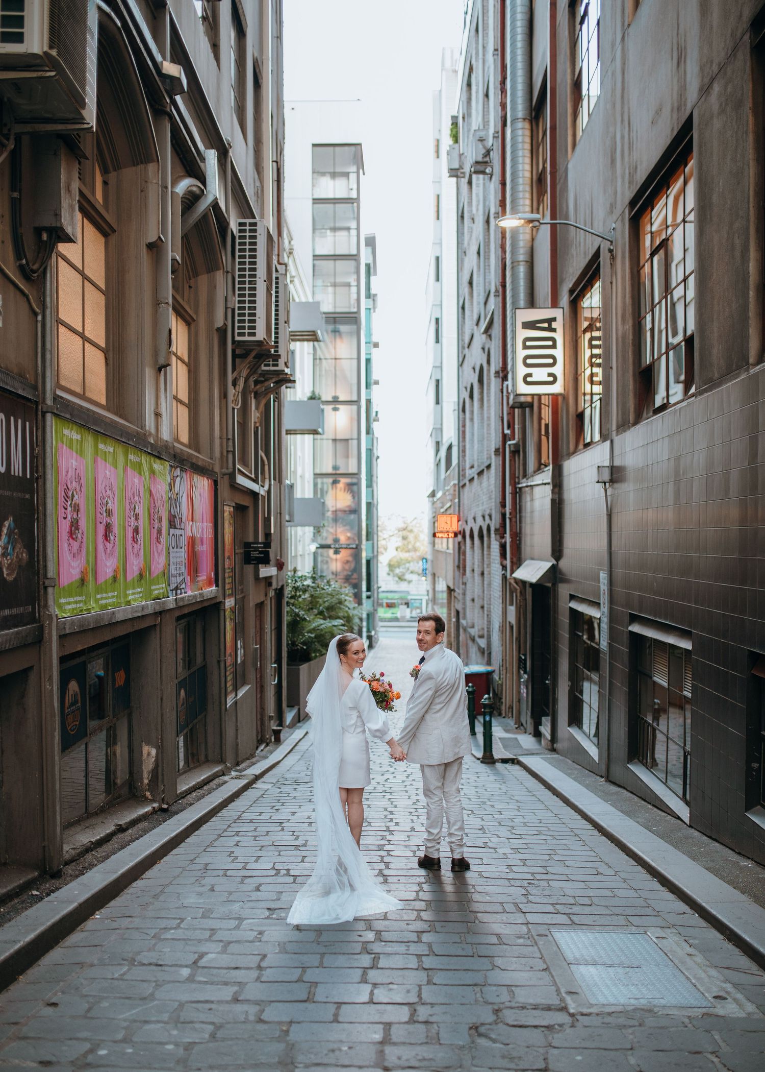 Bride and groom holding hands facing each other in charming cobblestone Melbourne city laneway.
