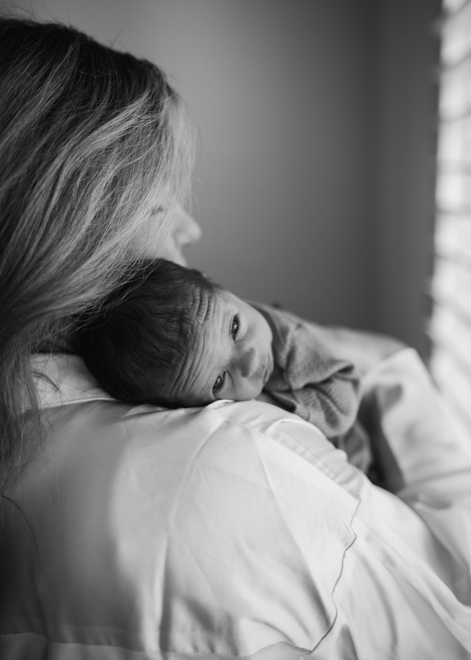 Black and white photo of a mother cradling her newborn baby on her shoulder.