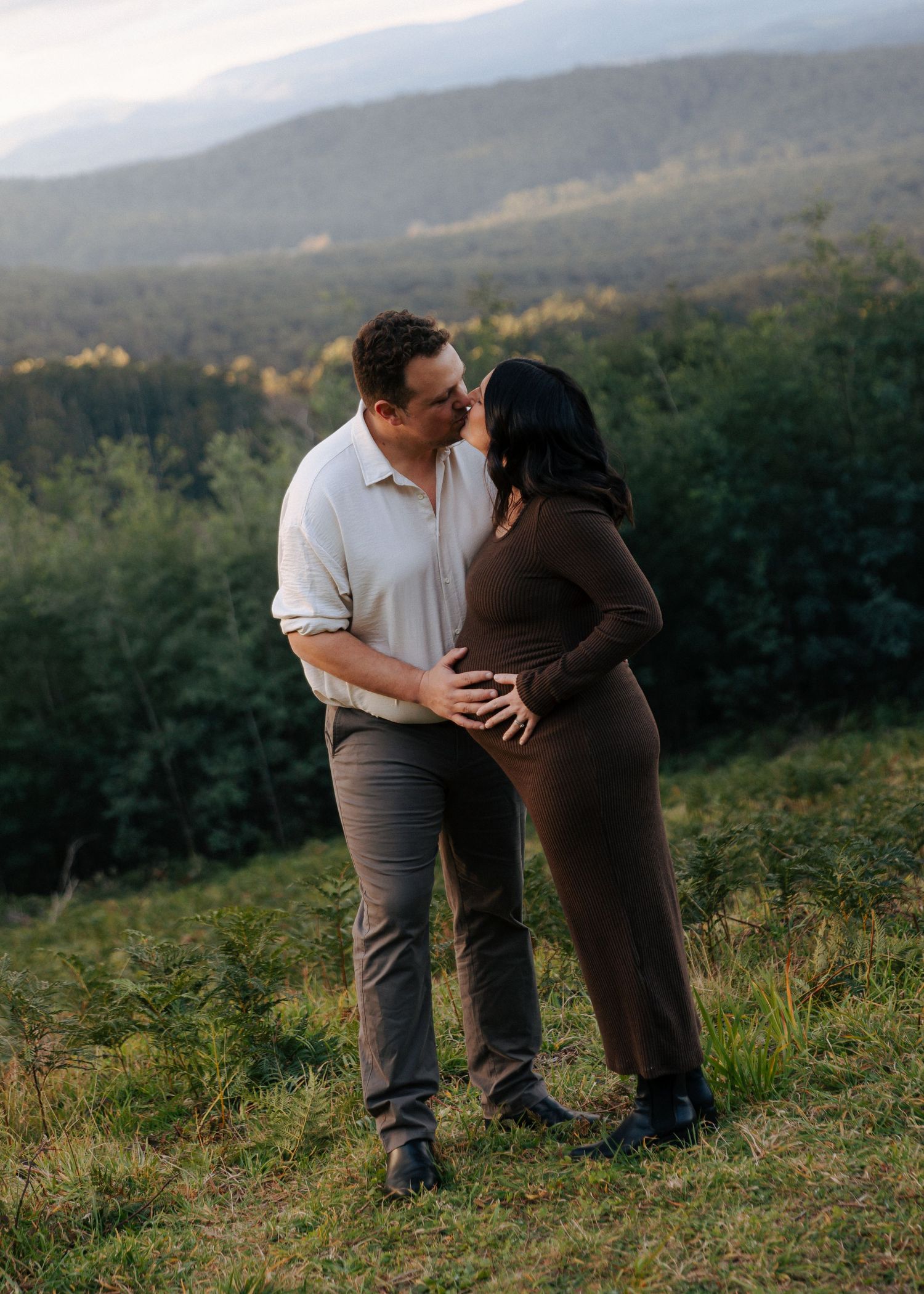 Couple sharing a kiss during outdoor maternity photoshoot with mountain views.