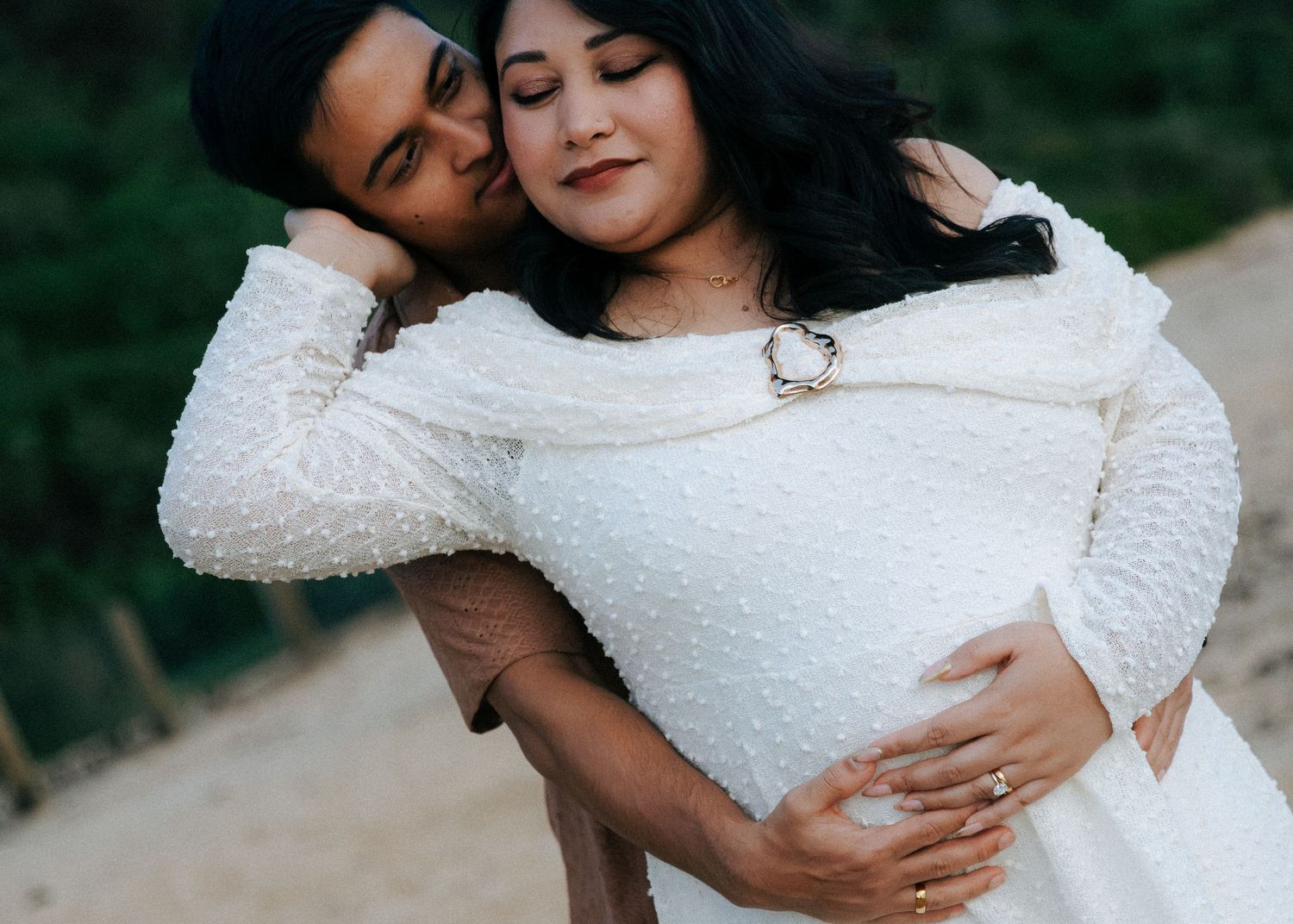 Close-up of couple embracing during maternity shoot, pregnant woman in white textured dress.