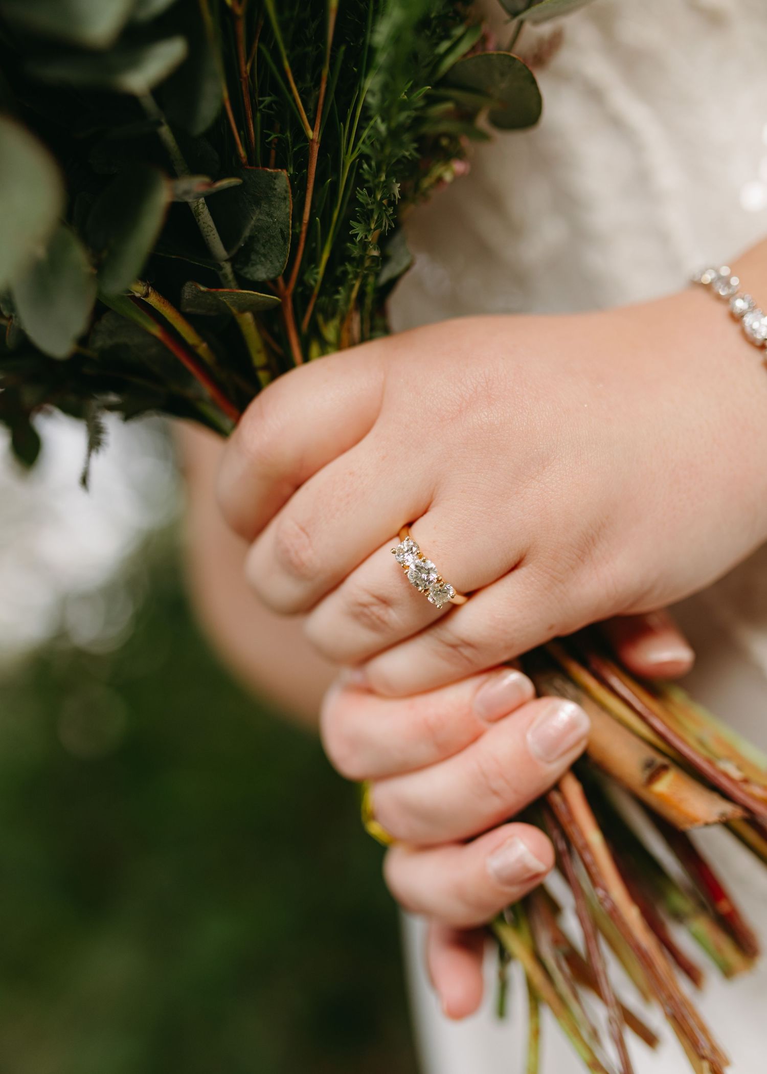 Close-up of bride's hand wearing a diamond ring while holding a green floral bouquet.