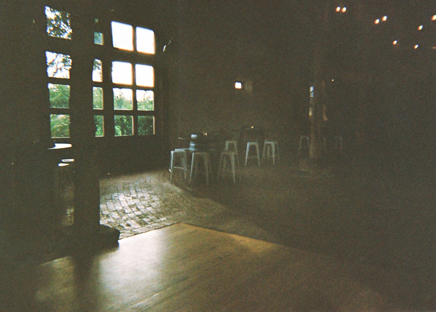 Dimly lit rustic wedding venue interior with wooden floors, large windows, and white stools.