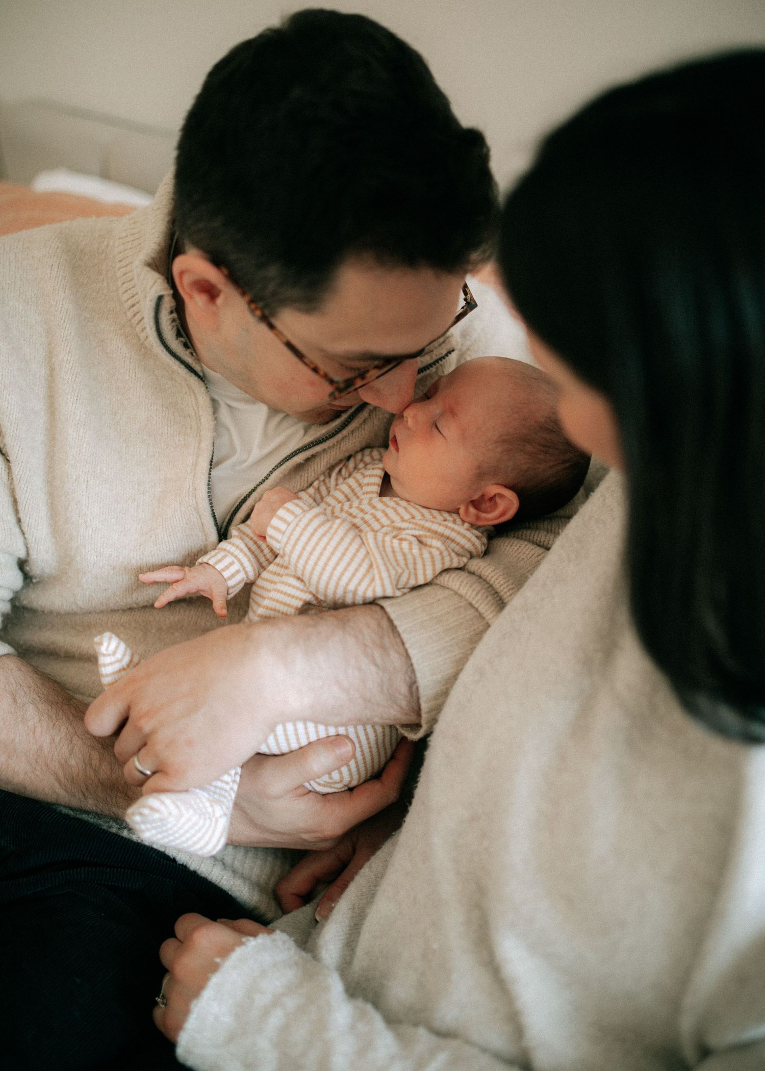 A father gently kisses his newborn baby while mother looks on tenderly during an intimate family moment.