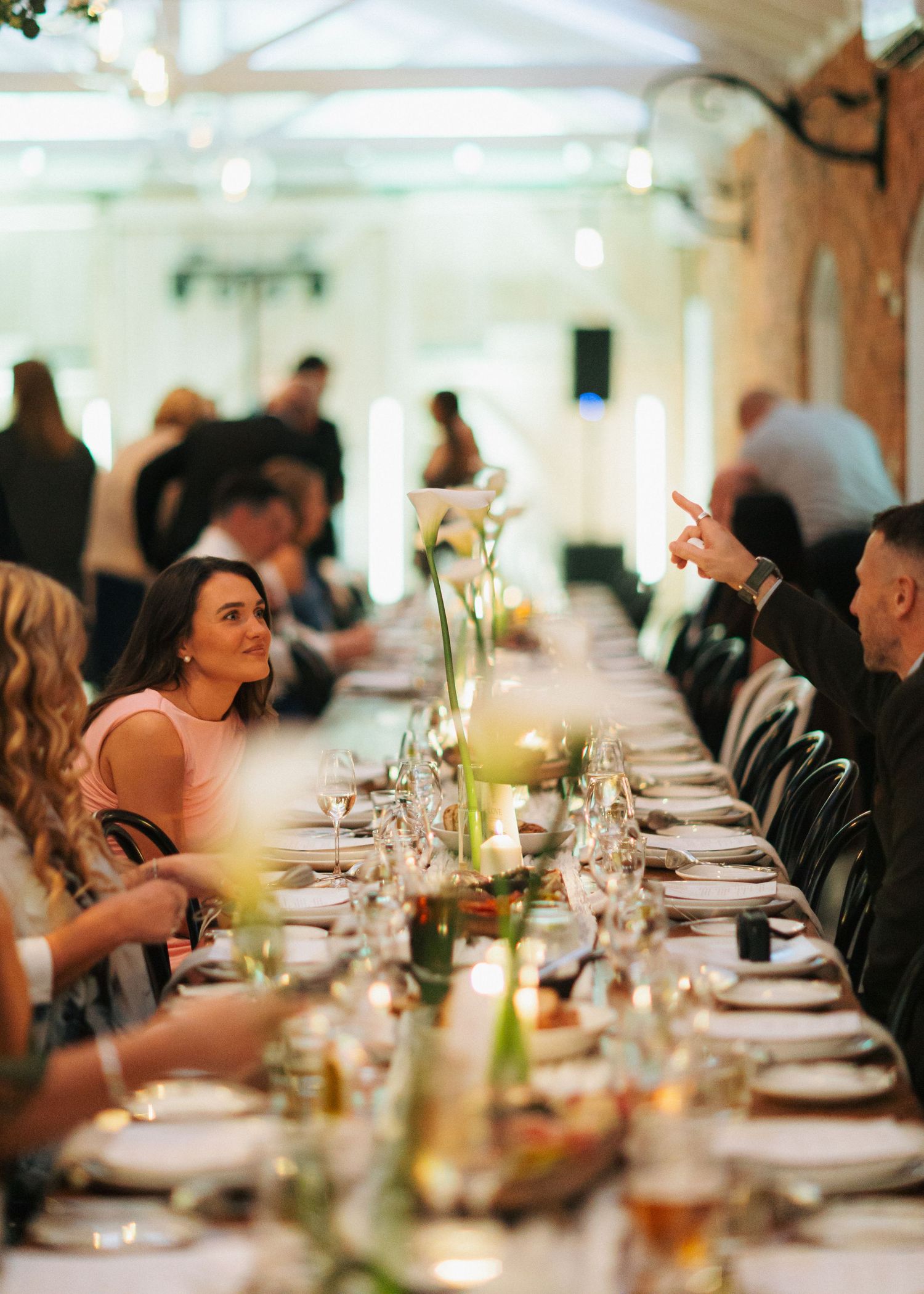 Elegant wedding reception dinner with guests seated at long decorated table with floral centerpieces.