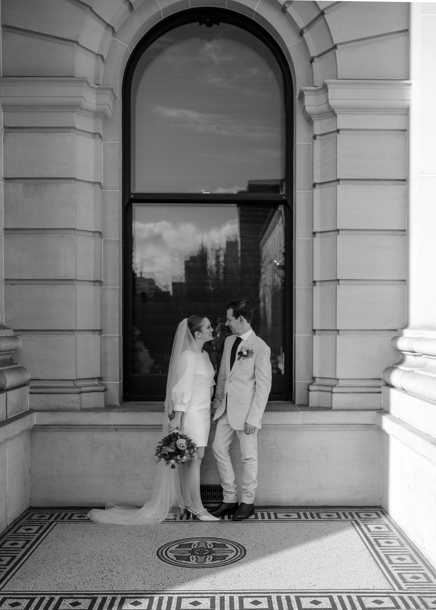 Black and white romantic portrait of bride and groom sharing intimate moment in arched building alcove.