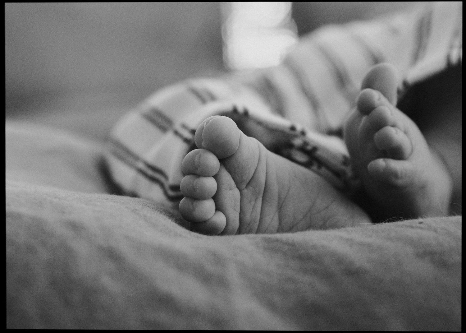 Black and white close-up of tiny newborn baby feet in striped pants.