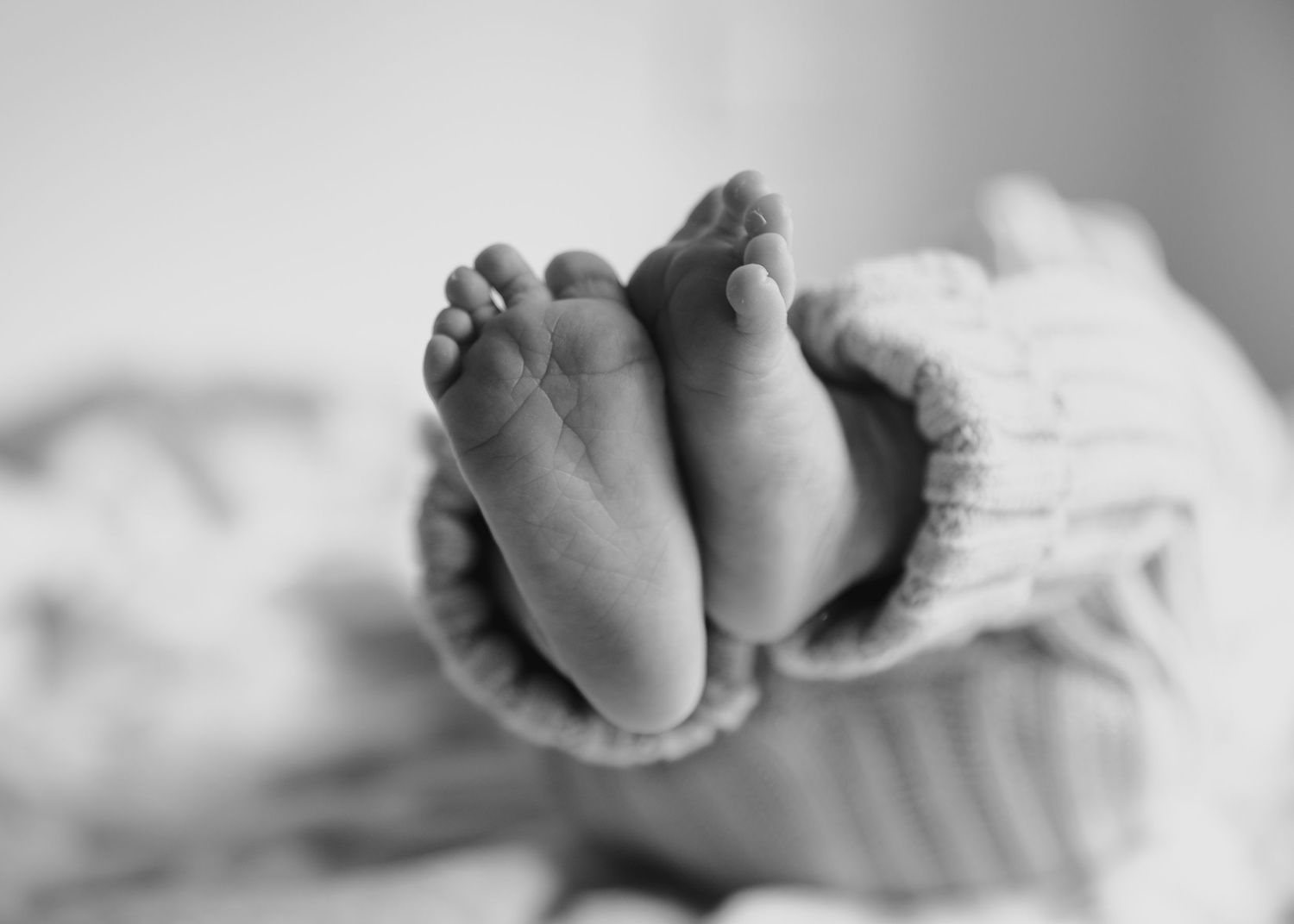 Black and white close-up of delicate newborn baby feet in a knit romper.