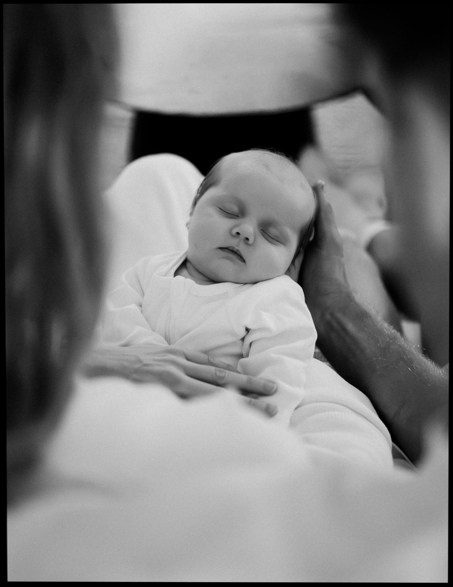 Black and white photo of sleeping newborn baby cradled in parents arms.