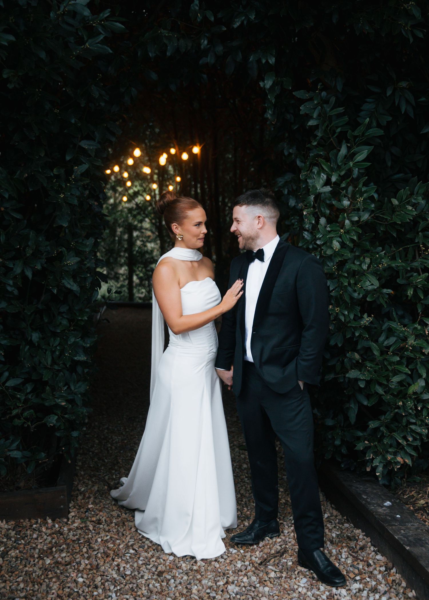 Bride and groom sharing romantic moment in garden at dusk.