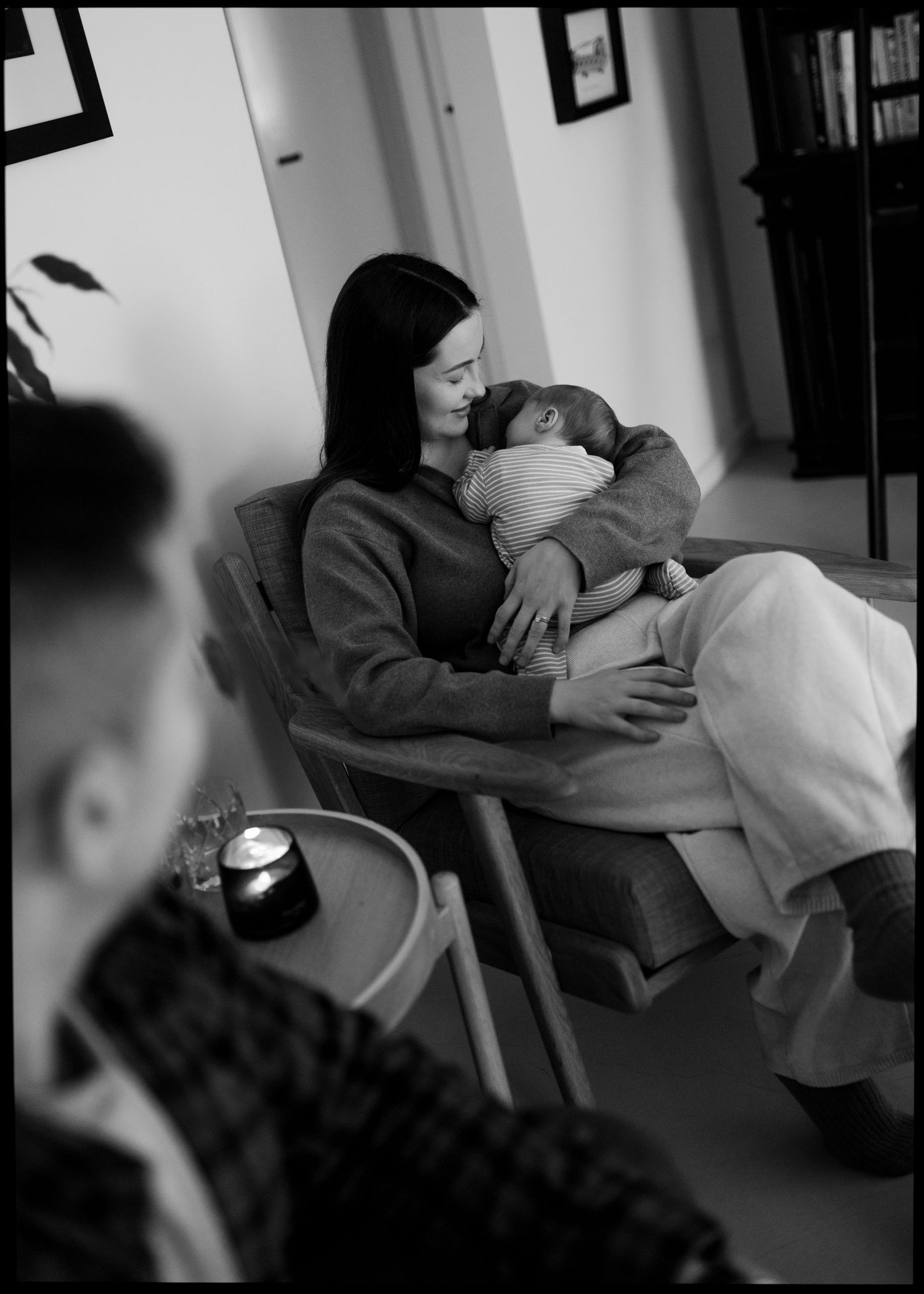 Black and white photo of a mother sitting and cradling her newborn baby indoors.