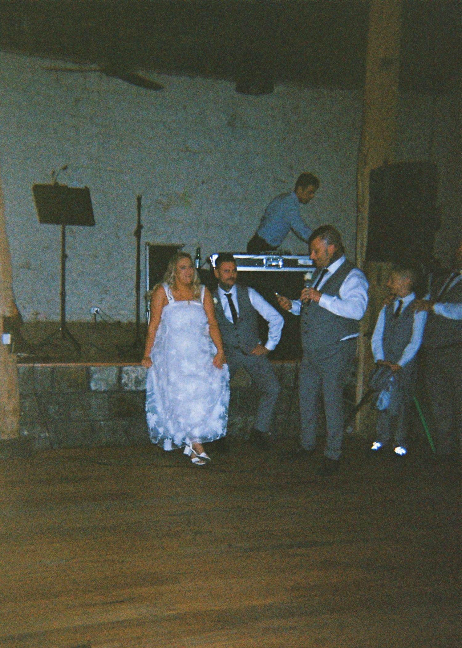 A bride in a white gown dances with groomsmen on a wooden dance floor at a rustic barn wedding reception.