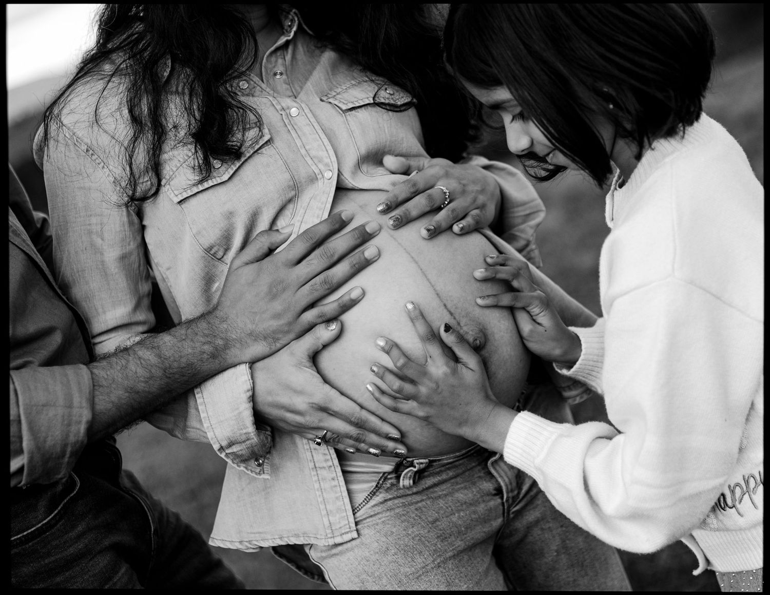 Black and white close-up of hands touching pregnant belly during maternity shoot.