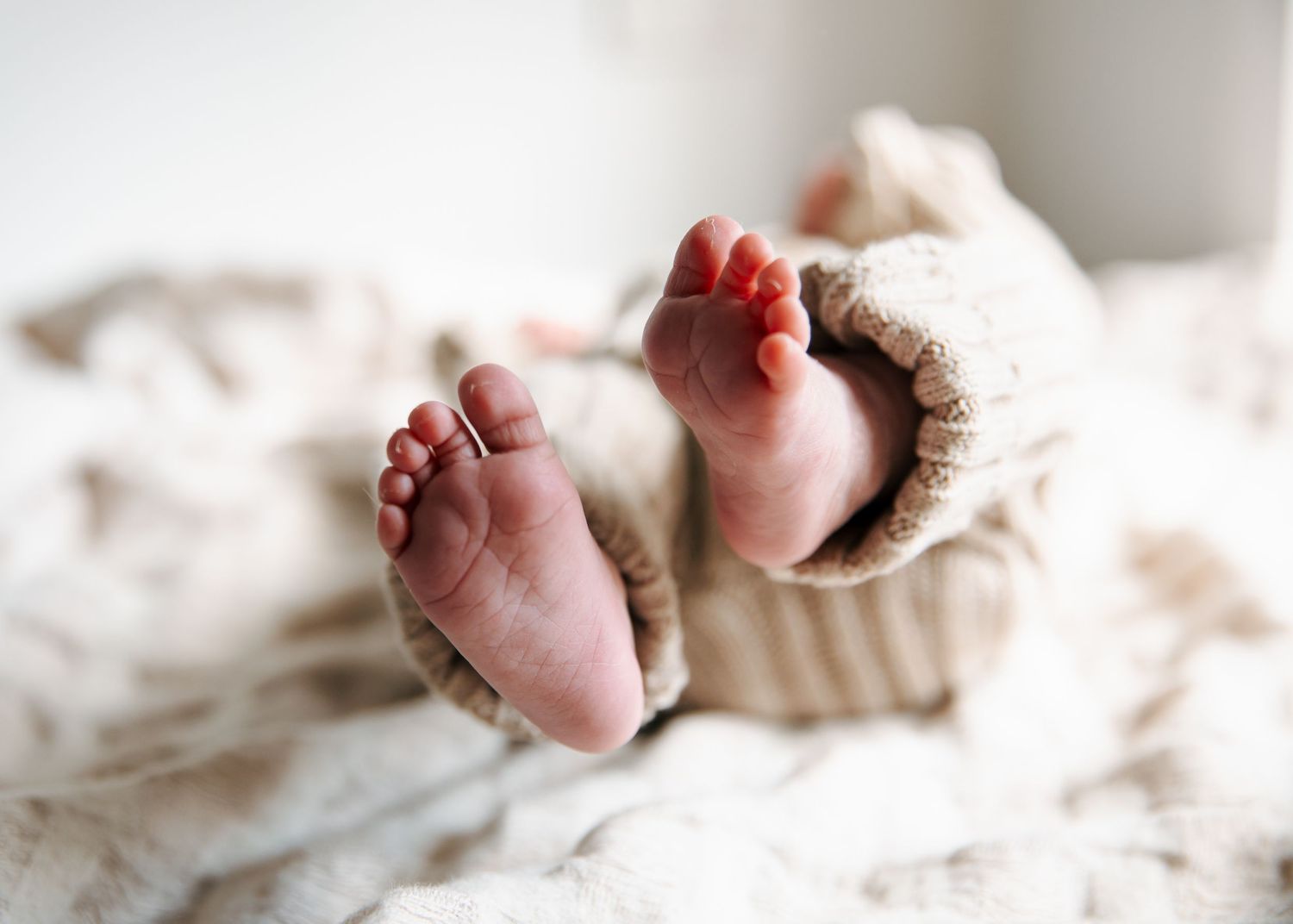Newborn baby's tiny feet in a striped knit romper on a soft white blanket.