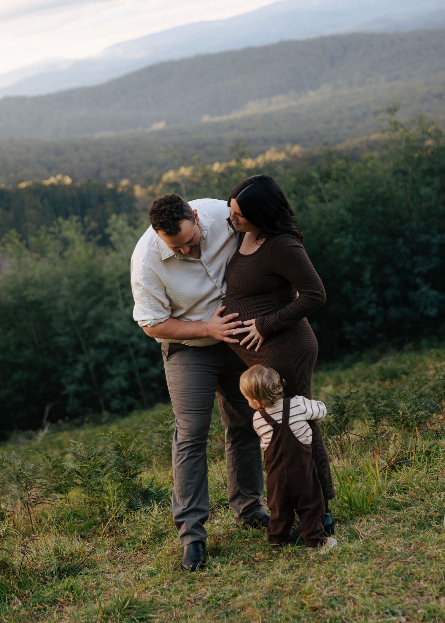 Couple and toddler sharing a tender moment together in a scenic field during maternity session.