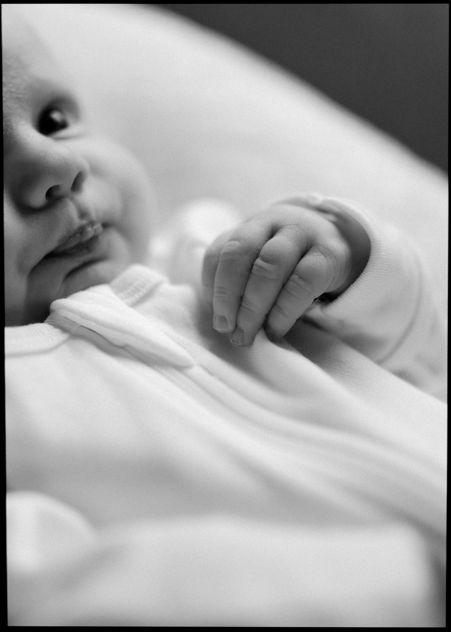Black and white close-up of peaceful newborn baby's face and tiny delicate hand.