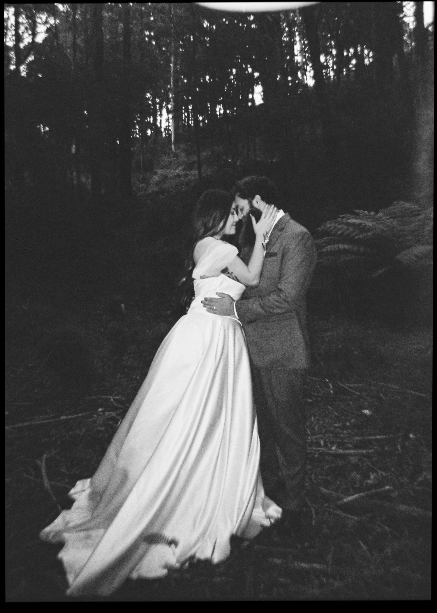 Black and white romantic portrait of bride and groom sharing an intimate moment kissing in a dark forest.