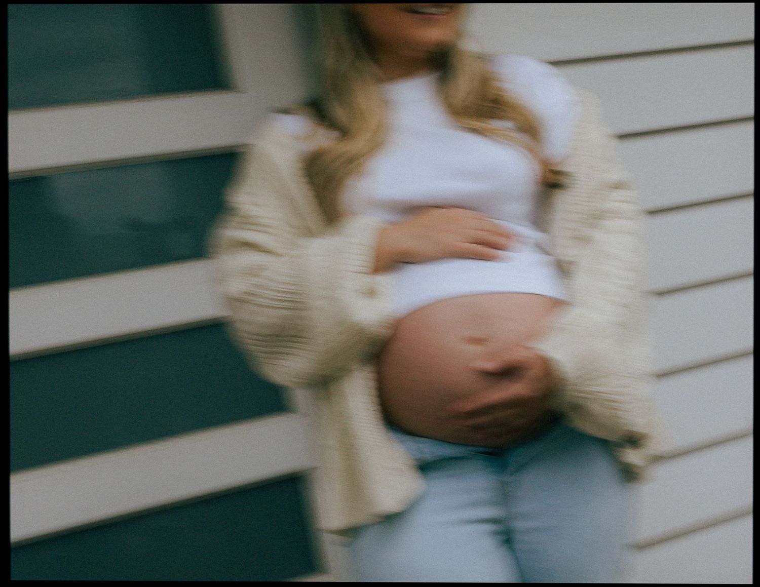 Close-up of pregnant woman in white crop top and jeans holding baby bump outdoors.