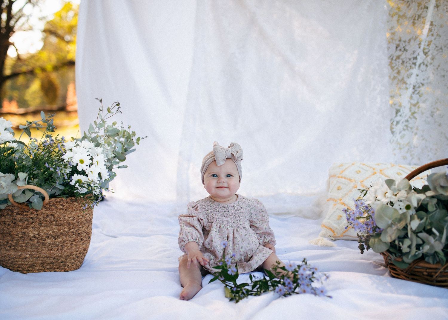 Adorable baby girl in floral romper sitting among flowers in boho outdoor setting.