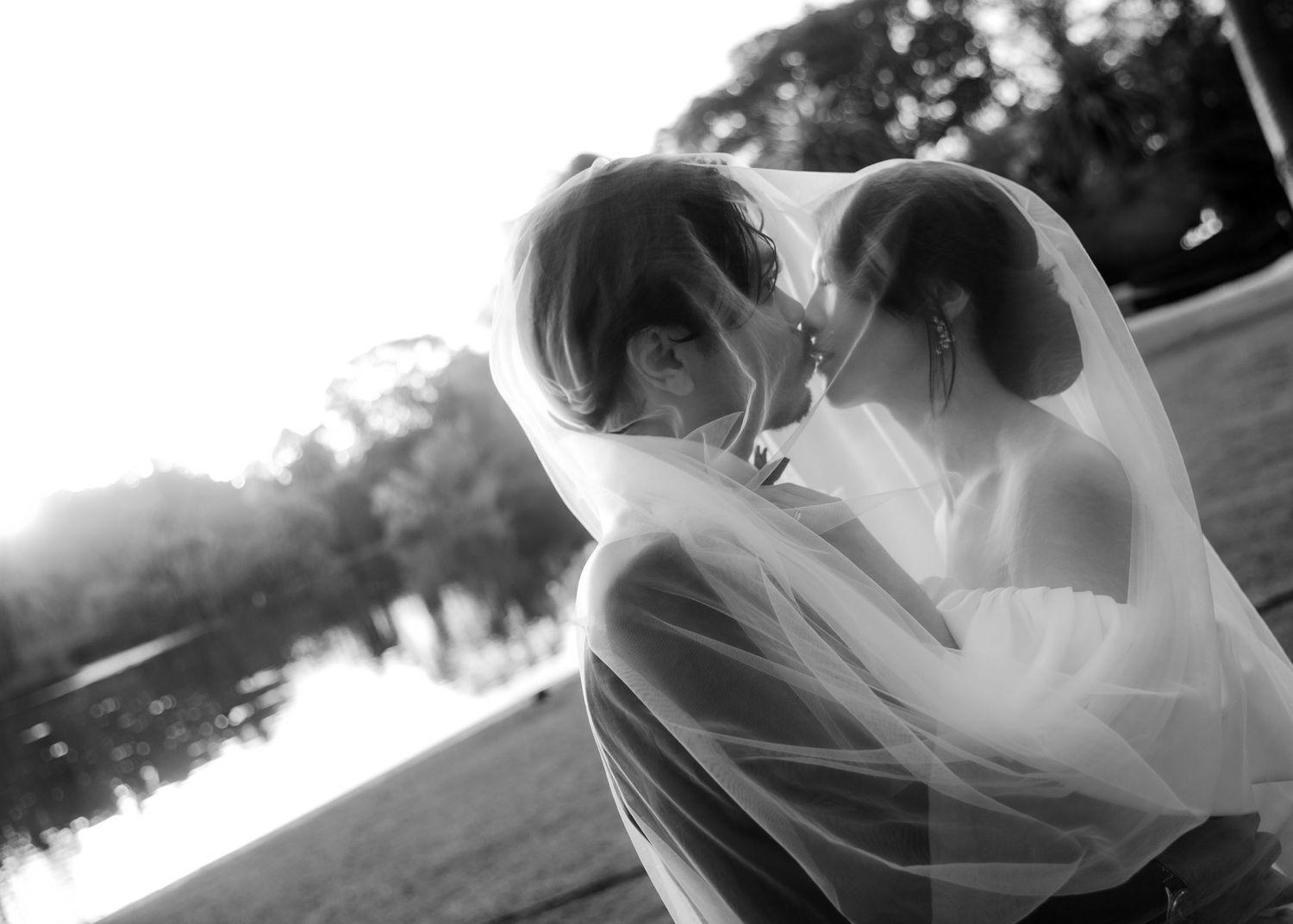 Black and white romantic photo of bride and groom sharing kiss under flowing veil.