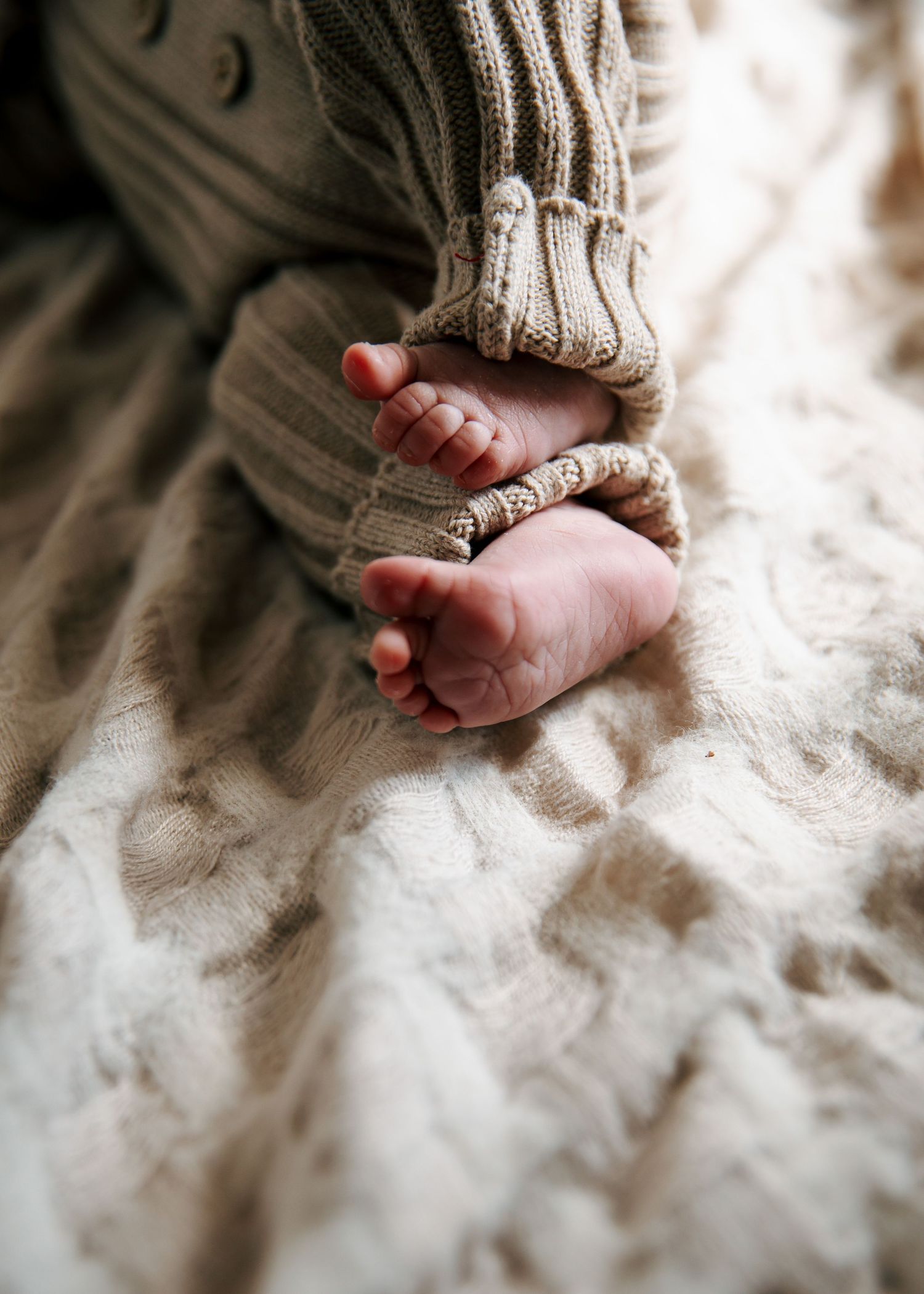 Close-up of newborn baby's tiny feet and hands on a soft textured blanket.
