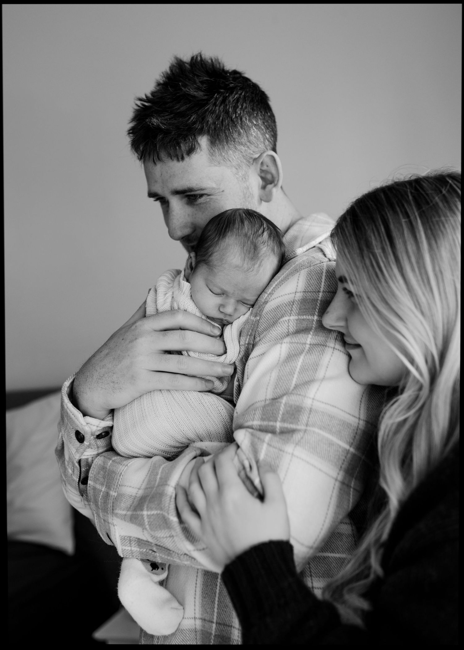 Black and white photo of father holding sleeping newborn while mother looks on tenderly.