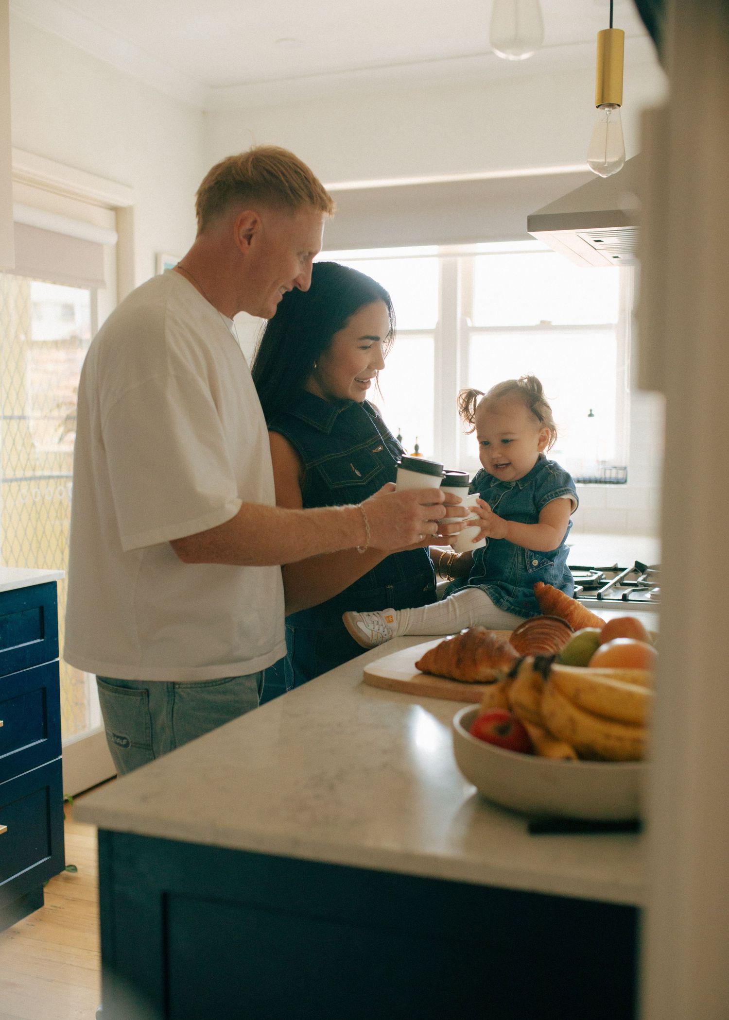Young family with baby enjoying time together in modern blue kitchen with fresh fruit.