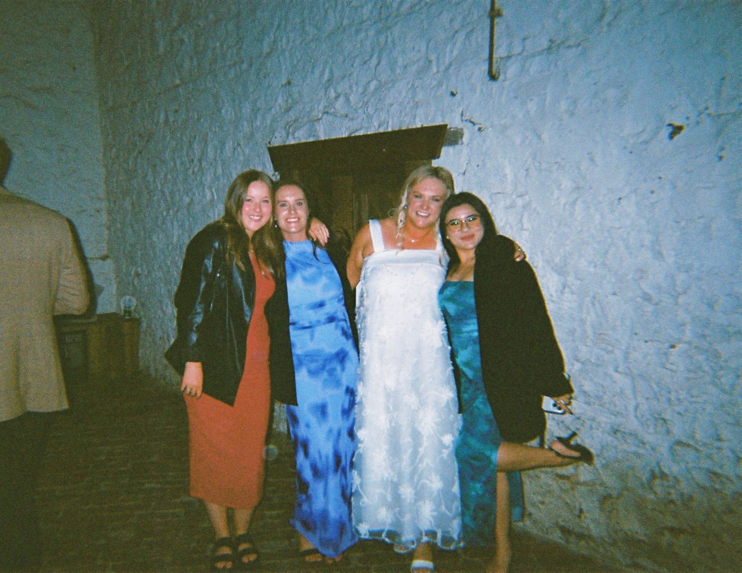 A bride in a white ruffled gown poses with three guests against a rustic stone wall at a wedding reception.