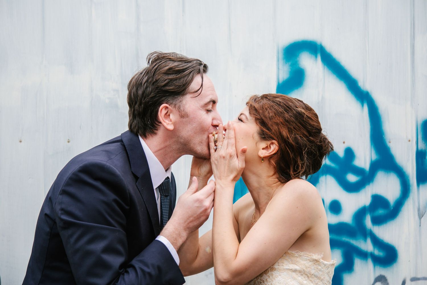 Bride and groom sharing a romantic kiss against a graffiti-painted wall.