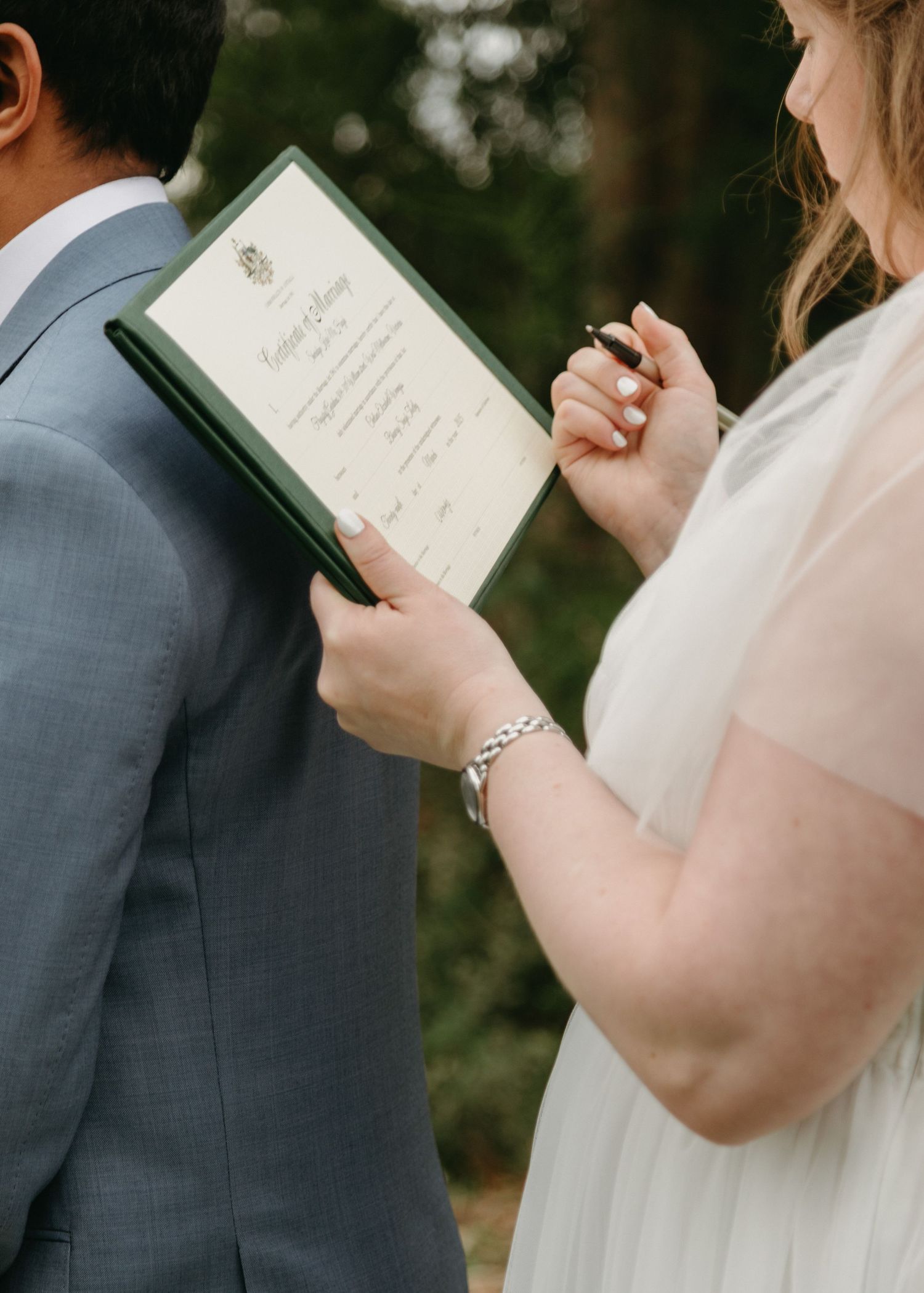 Bride in white tulle dress signing wedding certificate using groom's back as support.