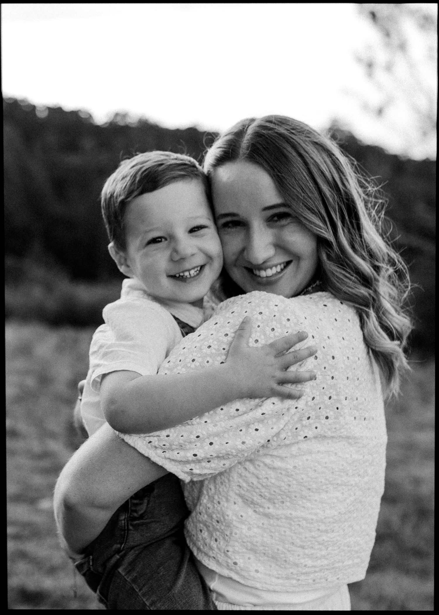 Black and white photo of a smiling woman holding a happy young boy outdoors.