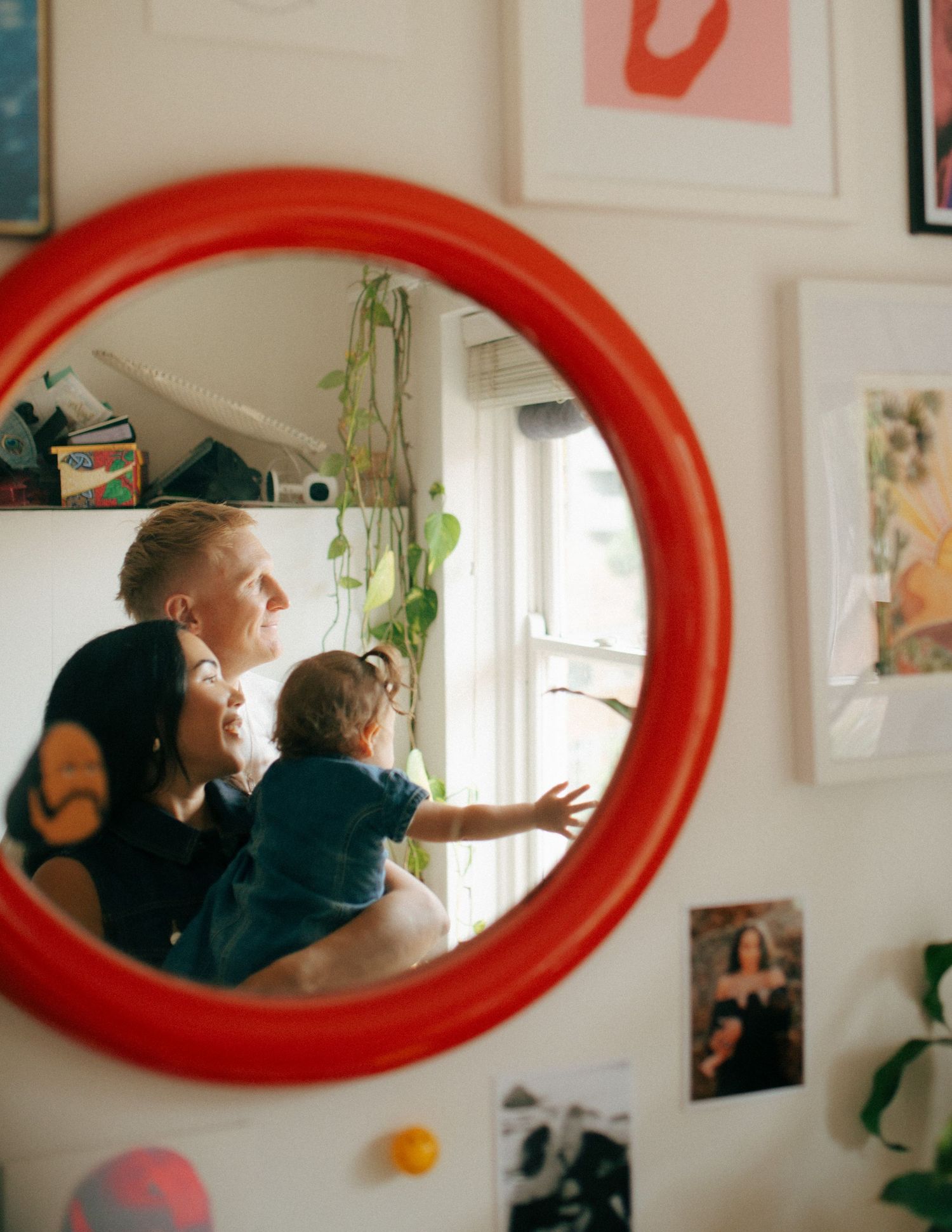 Family with baby reflected in round red mirror surrounded by colorful wall art.