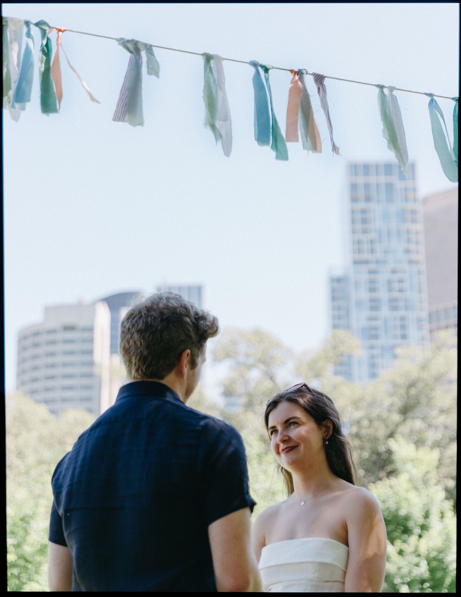 Couple sharing a romantic moment outdoors with colorful bunting overhead and city skyline in background.