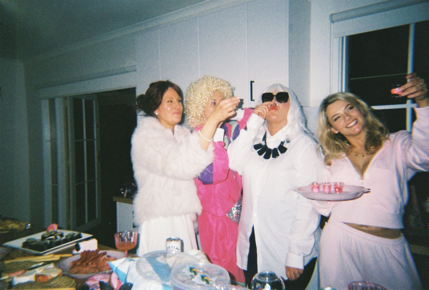 Four women in costumes including a bride and fluffy white outfits laugh together at a Halloween party.