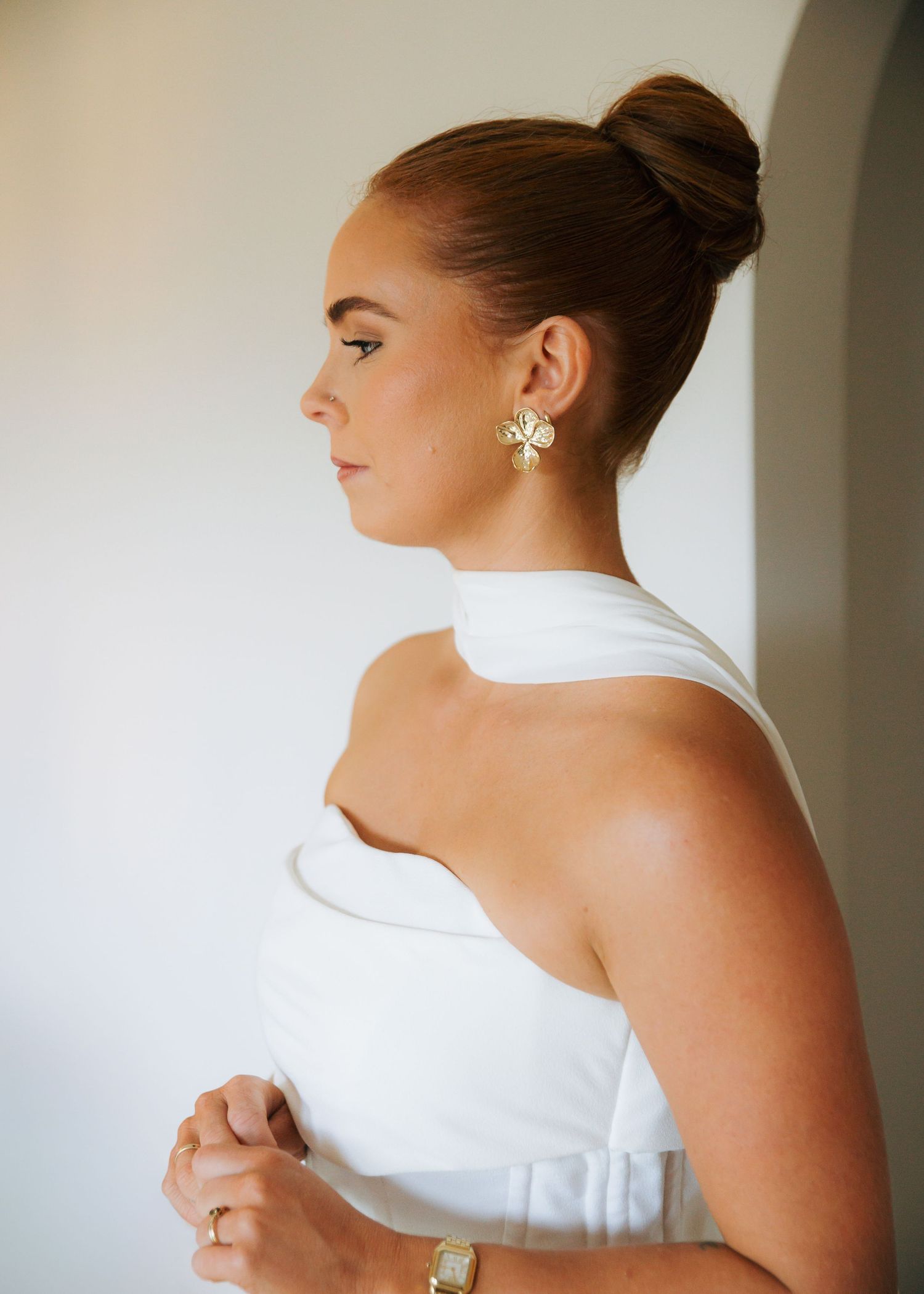 Close-up of bride in white halter gown wearing gold floral earrings and elegant updo.