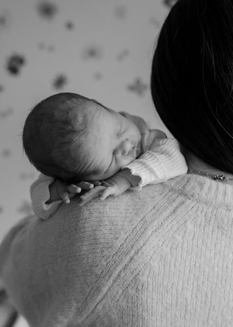 Black and white photo of newborn baby resting on parent's shoulder.