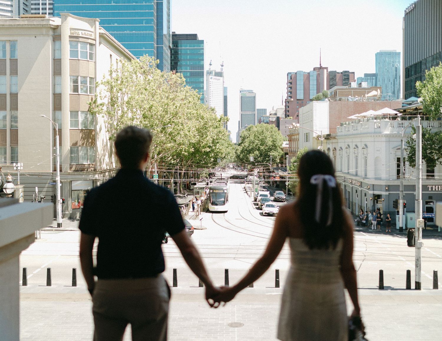 Couple holding hands in silhouette overlooking a busy city street during urban engagement photoshoot.