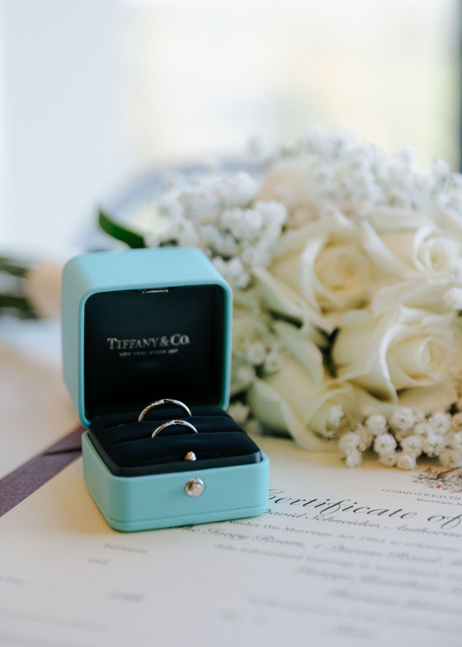 Tiffany & Co. wedding rings in iconic blue box beside white roses and baby's breath bouquet.