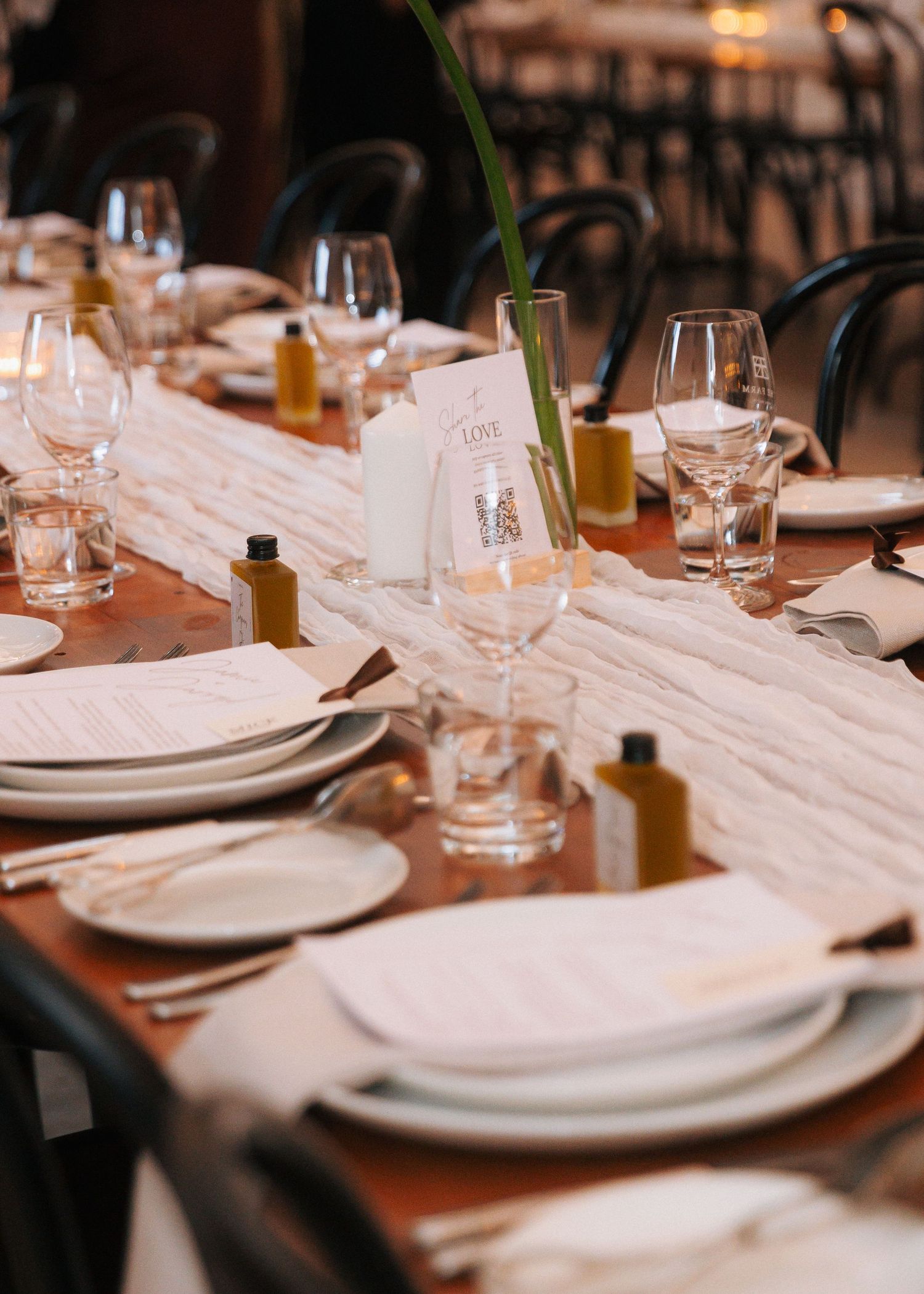 Elegant wedding reception table set with white linens, glassware, menus, and small olive oil bottle favors.