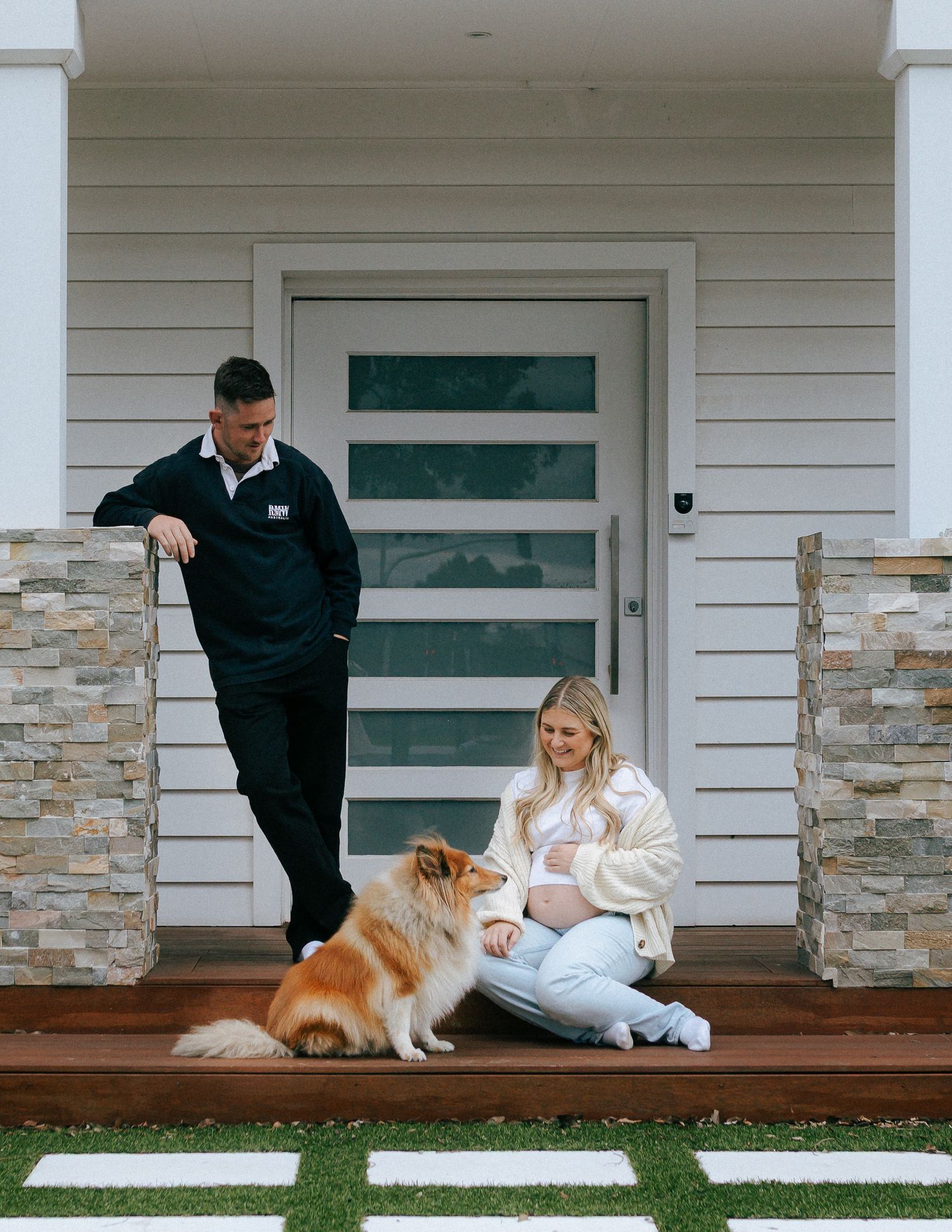 Couple with fluffy Collie dog sitting on front porch of modern white home.