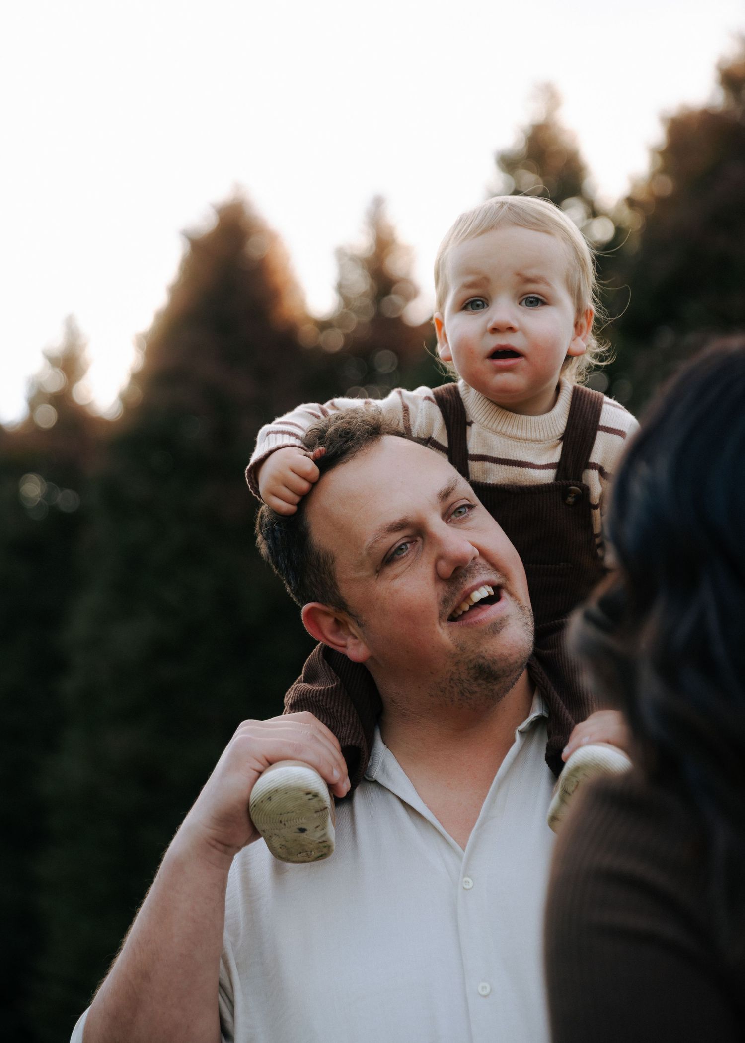 Close-up of toddler sitting on father's shoulders at golden hour outdoors.