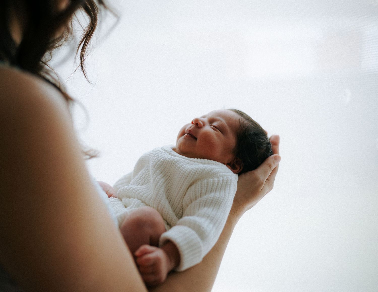 A mother gently cradles her peaceful newborn baby dressed in a white knit outfit.